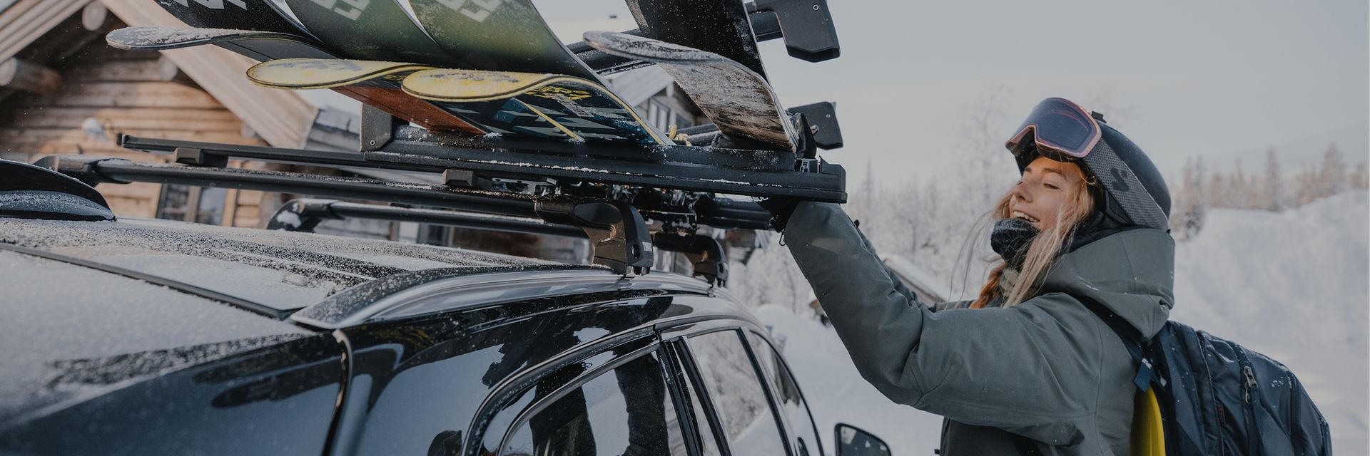Person loading skis onto a car with Thule ski racks in a snowy mountain setting.