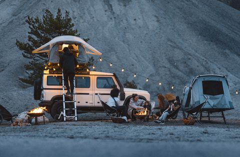 黃昏時分，人們圍坐在篝火旁，旁邊是兩輛裝有 Thule 帳篷和產品的汽車。