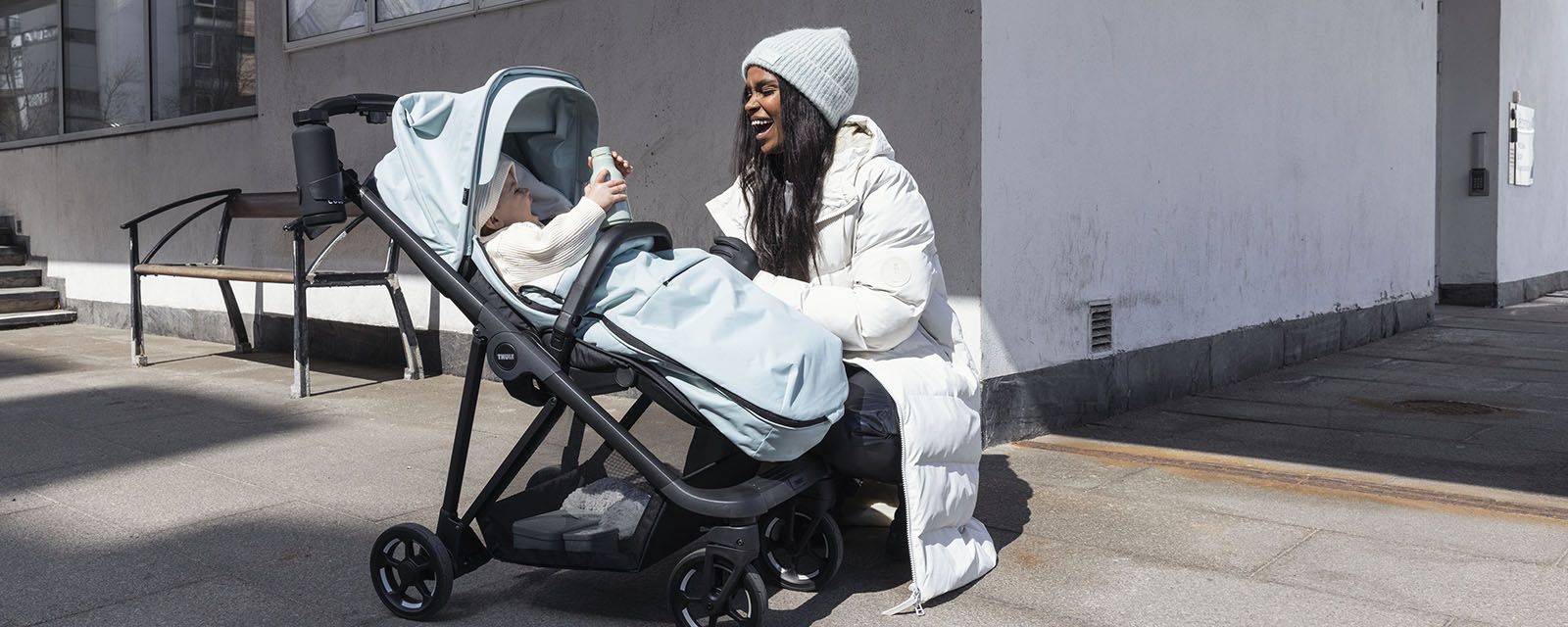 Una donna si china verso il suo bambino in un passeggino con un coprigambe.
