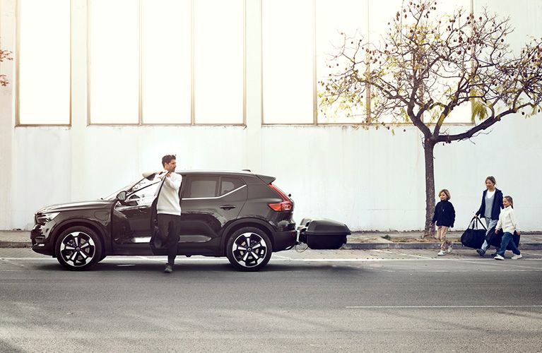 Un automóvil tiene un portaequipajes para barra de remolque Thule Arcos y un hombre sale del vehículo y su familia camina hacia él.