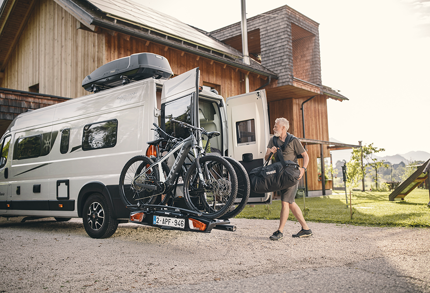 A man loads gear into a van with the rear door open and bikes on the Thule VeloSwing ven e-bike carrier.