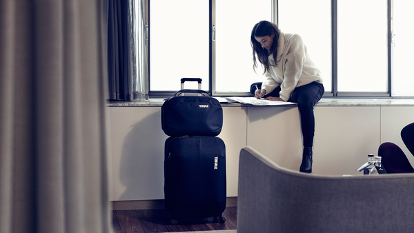 Una mujer se sienta en un hotel junto a una maleta y un maletín Thule Subterra.