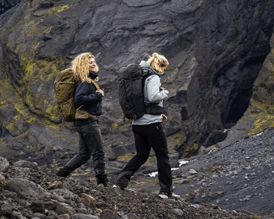 Dos mujeres caminan por un entorno volcánico con mochilas de senderismo de Thule.