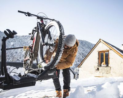 Xavier De Le Rue se zasněženými horami v pozadí připevňuje své zimní horské kolo na nosič kol Thule