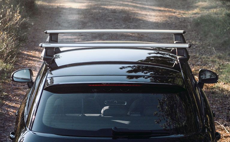 A car driving down a country road with a Thule Evo WingBar roof rack.