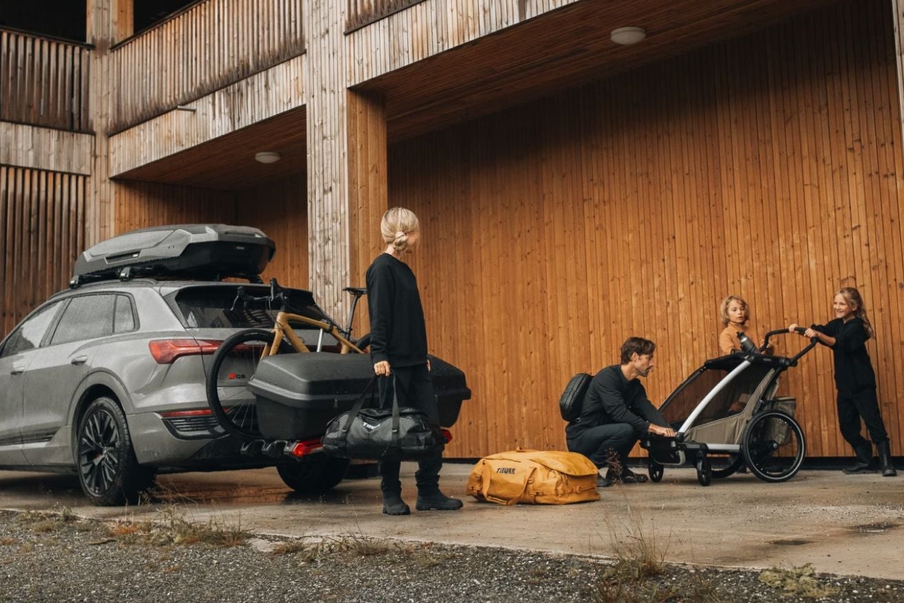 Familie packt Thule-Ausrüstung, Kindertrage und Gepäck in ein Auto mit Thule-Dachbox.