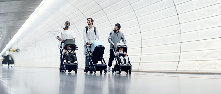 Tre pappor promenerar på en tunnelbanestation med kompakta Thule Shine barnvagnar.