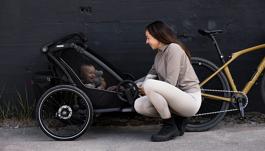 自転車トレーラーに乗った笑顔の子どものそばにひざまずく女性。