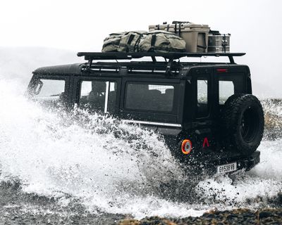 A vehicle drives through a puddle with a roof platform and gear on the roof.