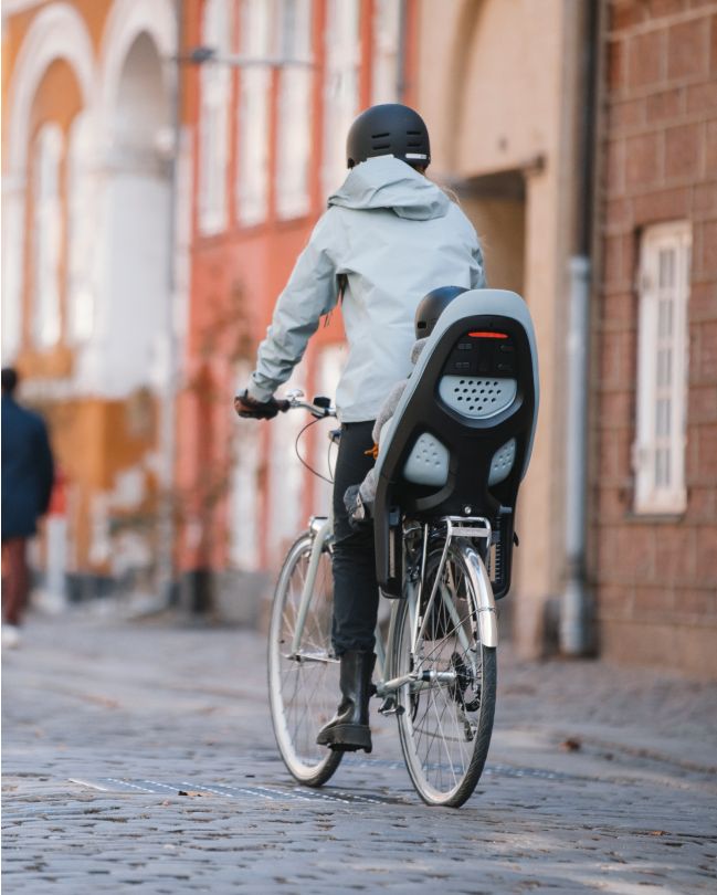 Une personne se déplace dans un environnement urbain sur un vélo auquel est fixé un siège de vélo pour enfant Thule Yepp.