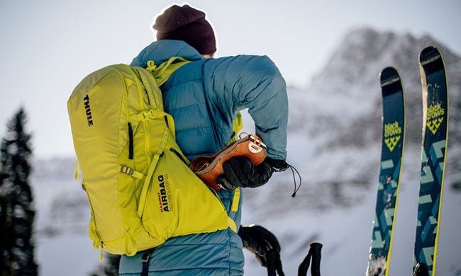 A close-up of a skier with their back to the camera, placing something in their Thule ski backpack.