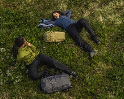 Two women lie in the grass with Thule hiking backpacks.