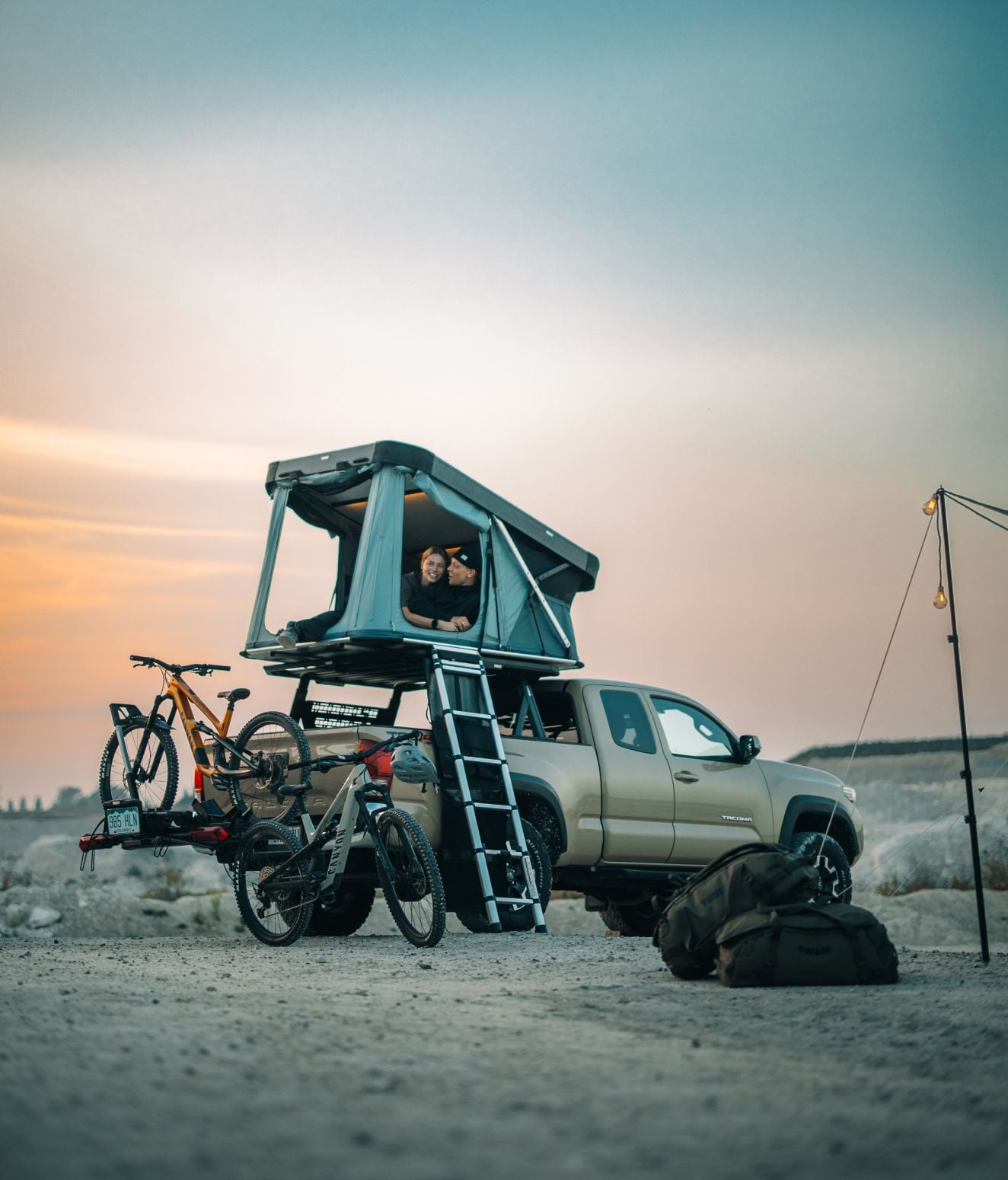 Car with Thule Widesky rooftop tent and bikes mounted, set up for camping in the desert at sunset.
