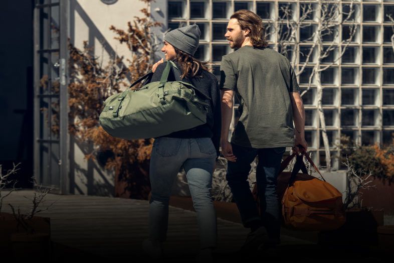 A couple walk towards a building with Thule duffel bags.