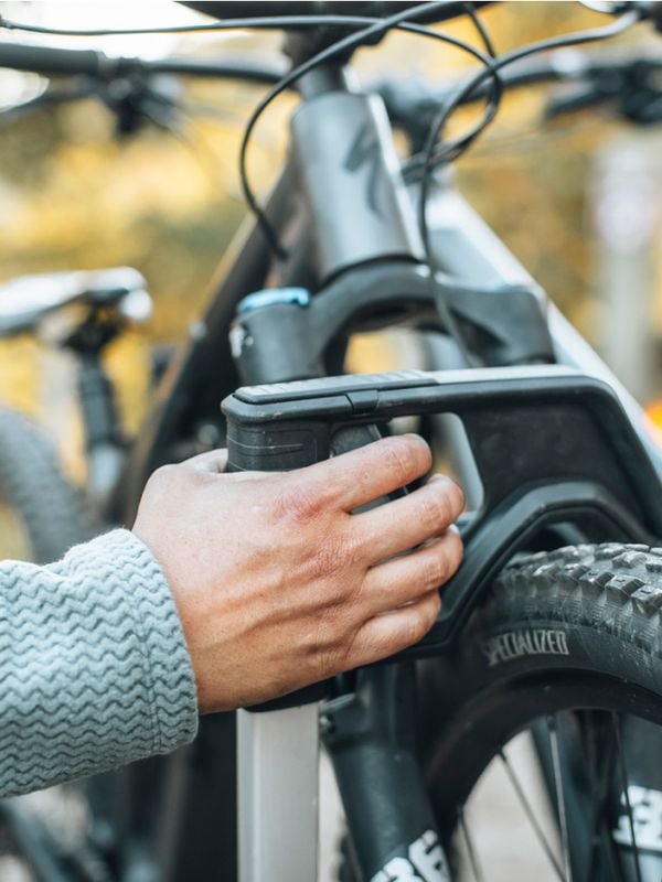 Nærbillede af hænder, der monterer en cykel på Thule Verse platform-cykelholderen, med flere cykler i baggrunden