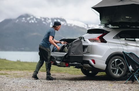 有人將裝備裝載到一輛裝有 Thule Onto 的汽車後座，停在山地景觀中。