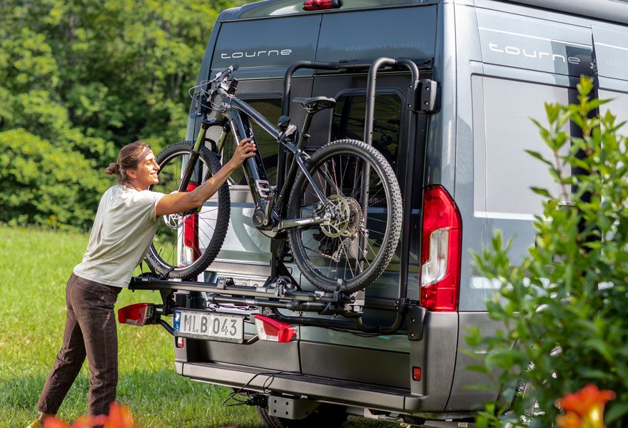 A woman unloads her bike from a Thule VeloTrack bike rack attached to her motorhome.