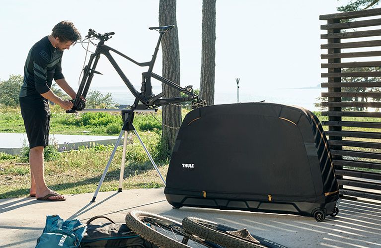 In his garden a man fixes a bike on a bike stand next to the Thule Round Trip bike travel case