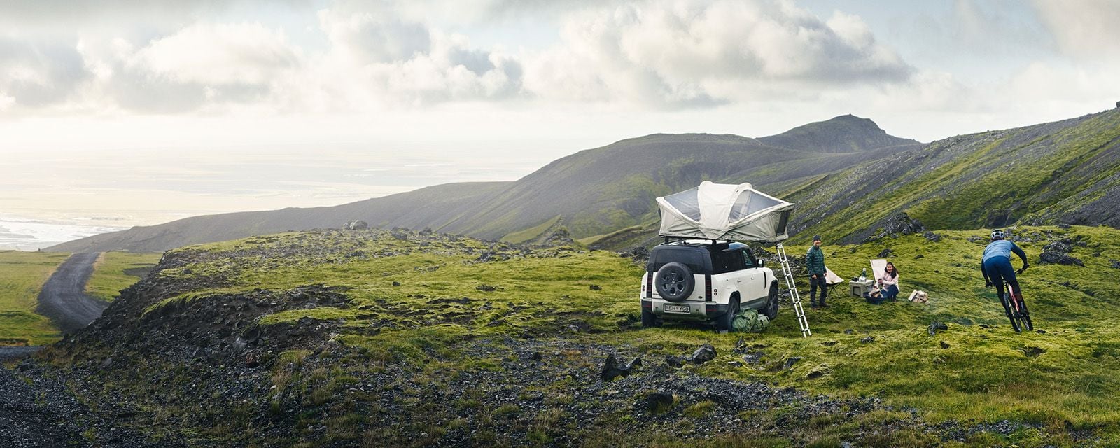 A vehicle in the foggy mountains has a Thule Approach roof top tent and cyclists around it