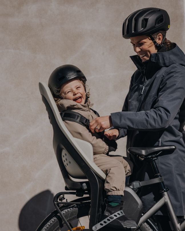 Parent cycling with a child in a Thule child bike seat.
