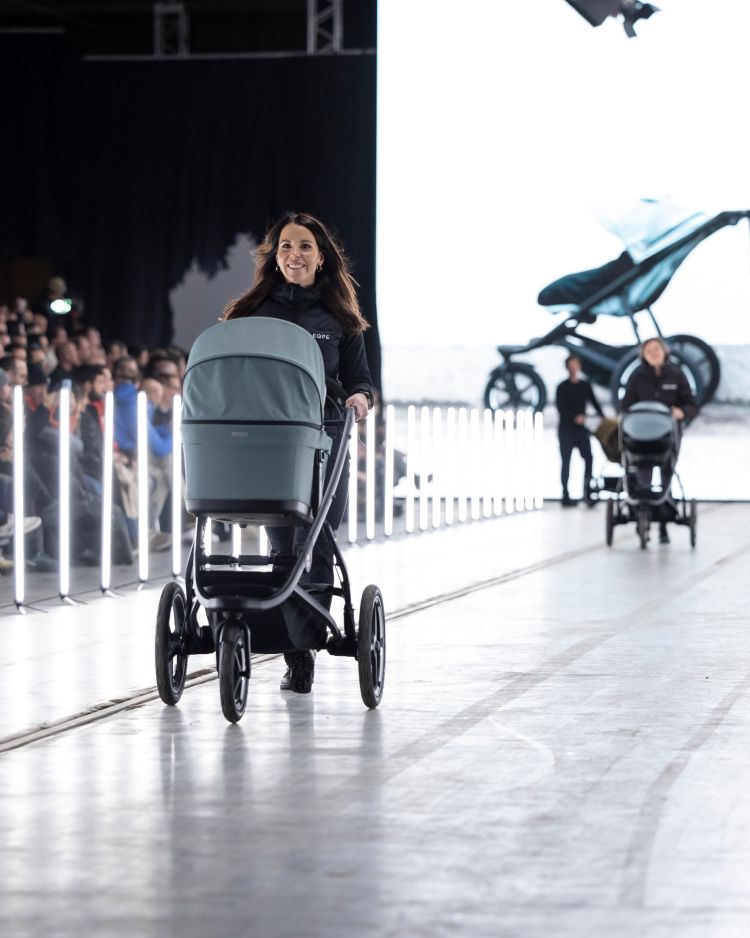 A woman walking down a fashion runway with a Thule Urban Glide 3 stroller in mid-blue.