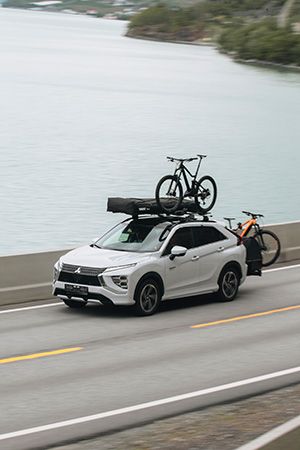 Cyclists unload a Thule rear cargo carrier from a EV with roof bike rack and bikes on top.