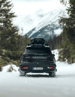A dark SUV with a roof box and a rear-mounted cargo carrier driving along a road.