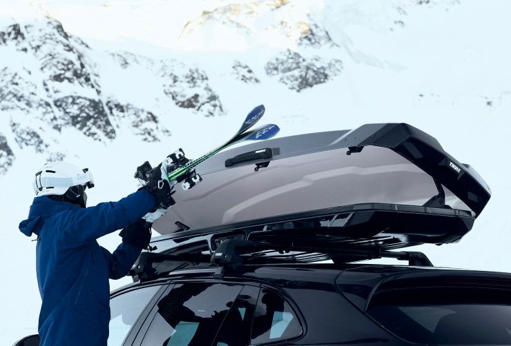 A close-up of a person loading their skis into a Thule ski box.