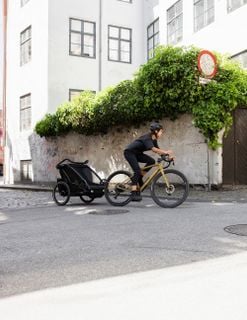 A person rides a bike while towing a child trailer on a quiet city street.