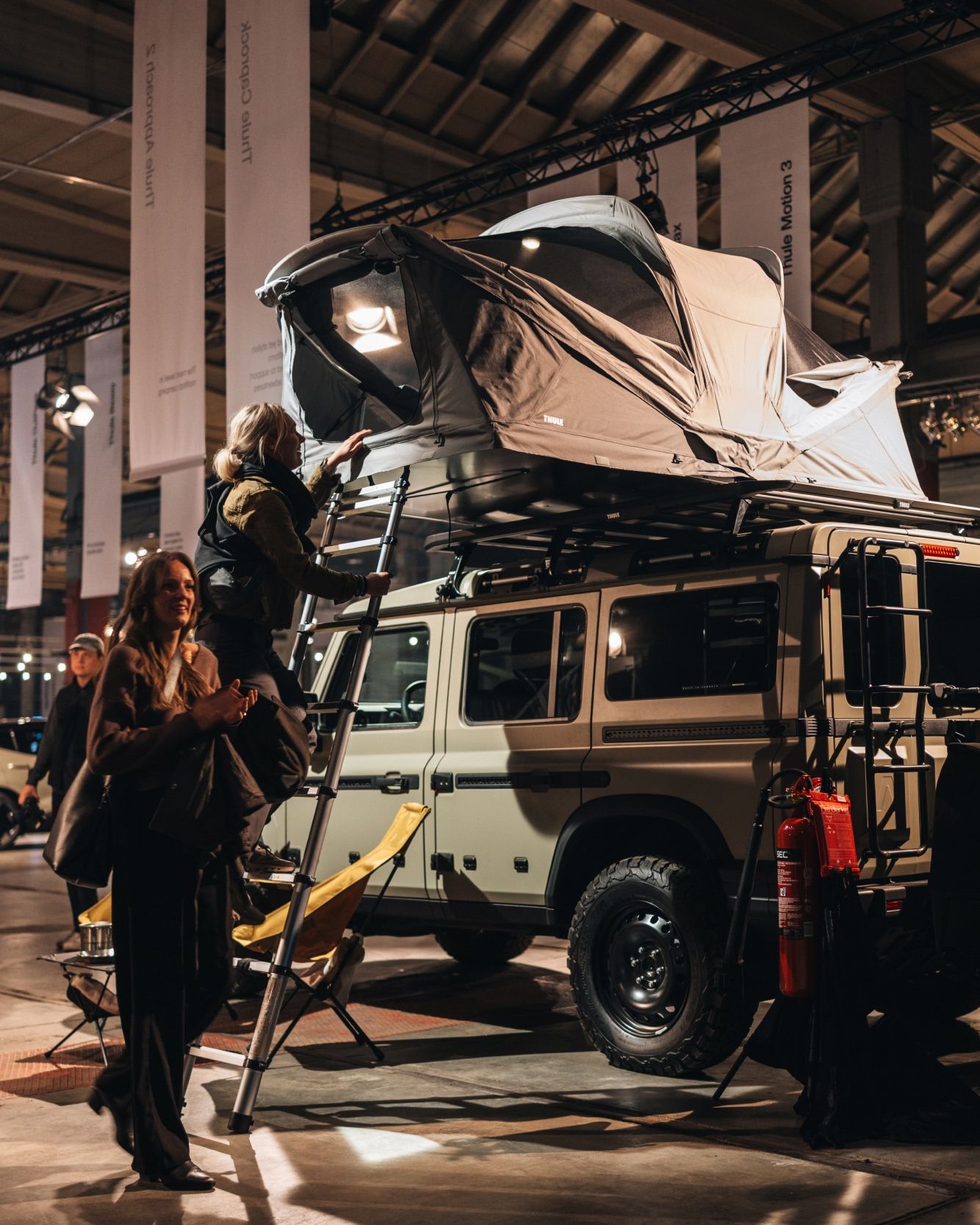 People exploring a rooftop tent on a parked vehicle indoors.