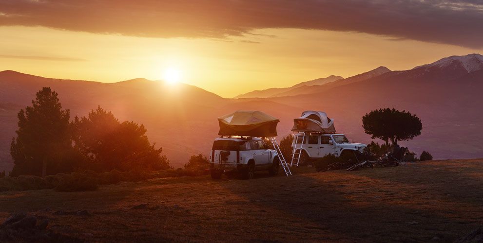 Twee jeeps met Thule Approach daktenten staan geparkeerd in een berglandschap met zonsondergang.