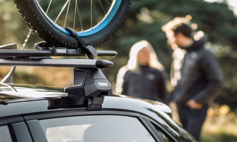 Close up of the Thule Evo WingBar roof racks with a roof bike rack attached and a couple in the background.