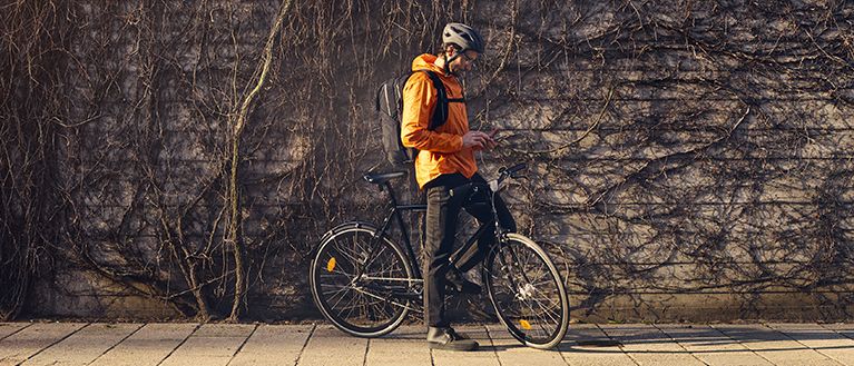 一位穿着橙色衣服的男士背着 Thule Paramount 自行车背包在城市街道上骑行。