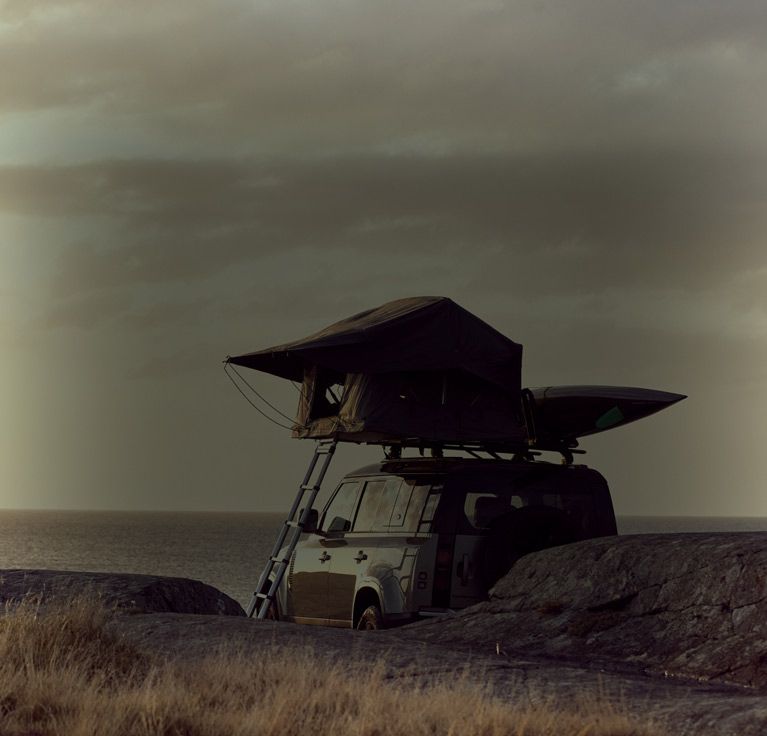 Man by the ocean loads his surf board on a car with a Thule Tepui Foothill roof top tent.