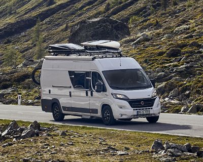 An rv with sup boards on the roof drives down a mountain path.