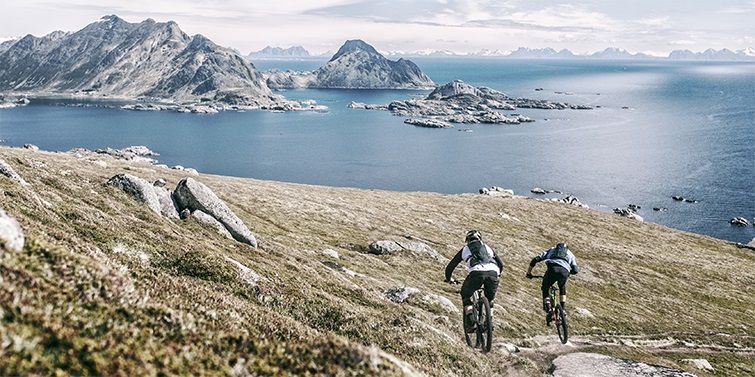 Two cyclists with hydration backpacks cycling next to a breathtaking mountainous archipelago.