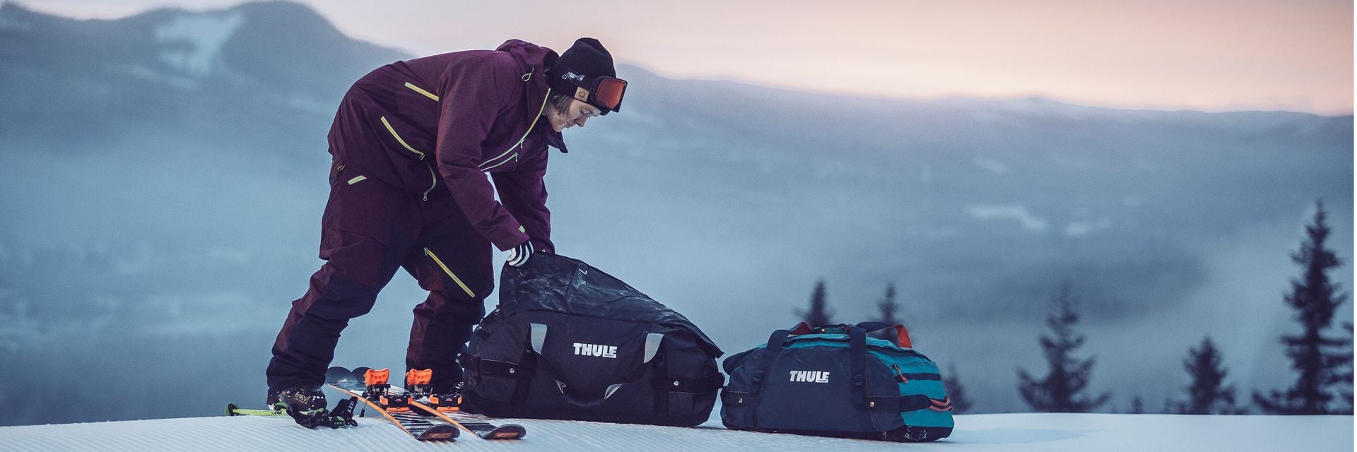 Person in Skiausrüstung, die Thule-Taschen auf einer verschneiten Piste packt.