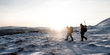 Two people hiking with Thule backpacks on a snowy mountain.