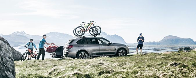 Une voiture blanche roule sur une autoroute le long d&#x27;un lac, avec une tente de toit, un v&#xE9;lo et un porte-v&#xE9;los sur boule d&#x27;attelage.