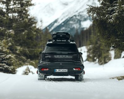 A dark SUV with a roof box and a rear-mounted cargo carrier driving along a road.