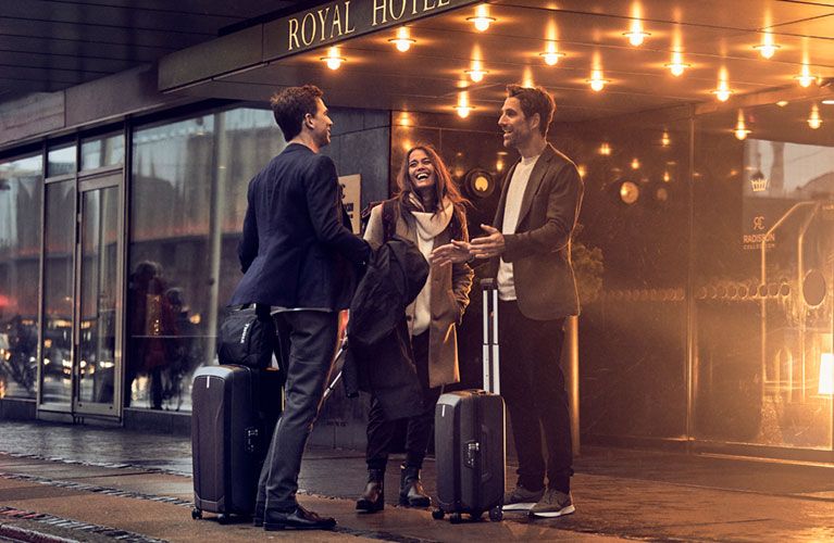 Three people stand chatting and laughing outside of a hotel with Thule suitcases.
