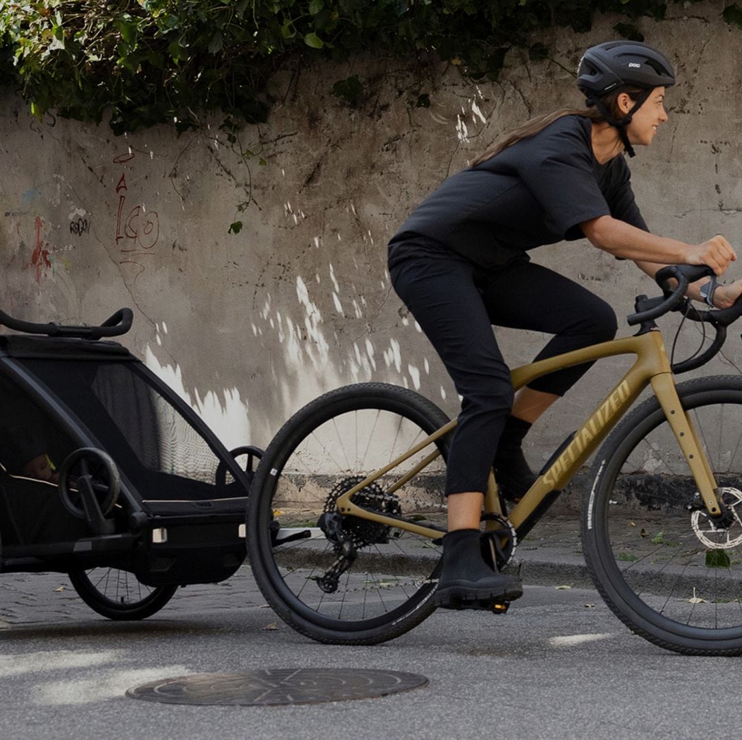 A woman rides a bike down a city street while towing a Thule bike trailer.