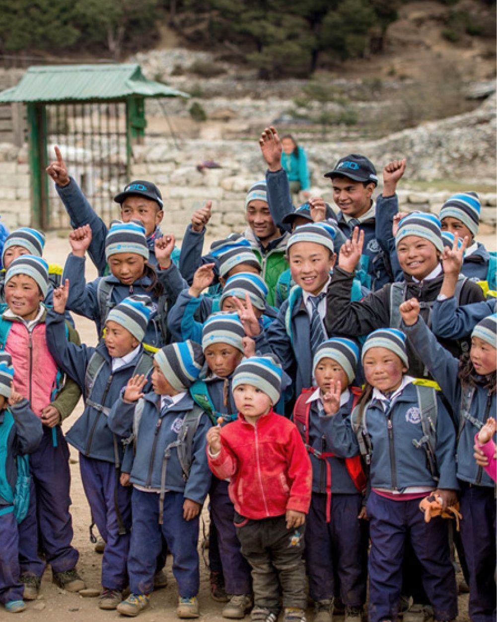 A group of children smile and wave to the camera.