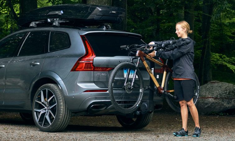 In a forest a woman loads her Thule Apex XT hitch bike rack with a bike.