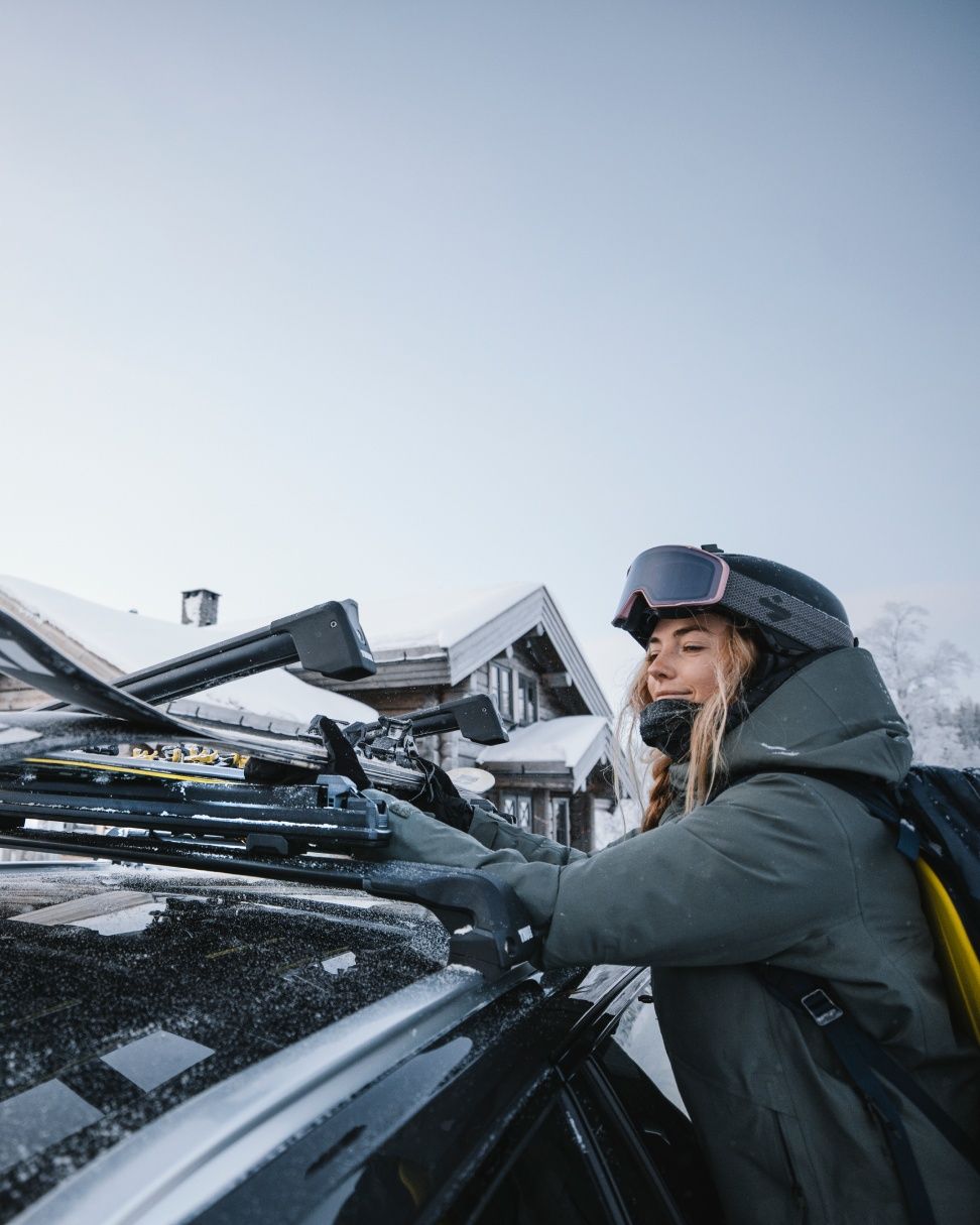 A woman loads her skis onto a vehicle with Thule Ski Racks on the roof.