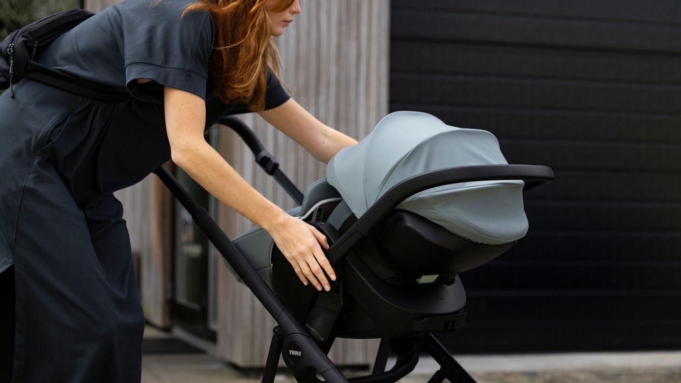 ベビーカーからThule Maple乳児用チャイルドシートのクリップを外そうと手を伸ばす人。