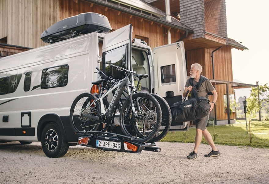 A man loads items into the back of his motorhome that has the Thule Veloswing installed.