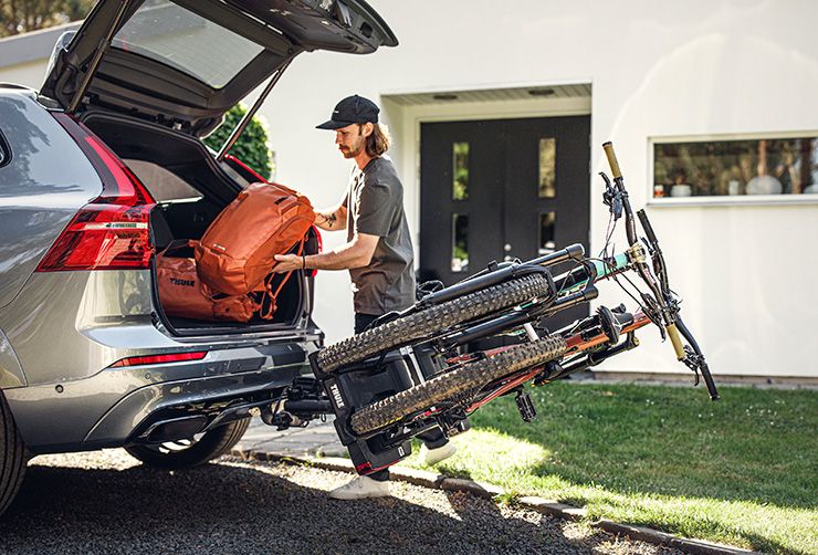 Ein Mann lädt eine Reisetasche in den Kofferraum seines Autos, während die Fahrräder auf seinem Thule EasyFold XT noch geladen sind.