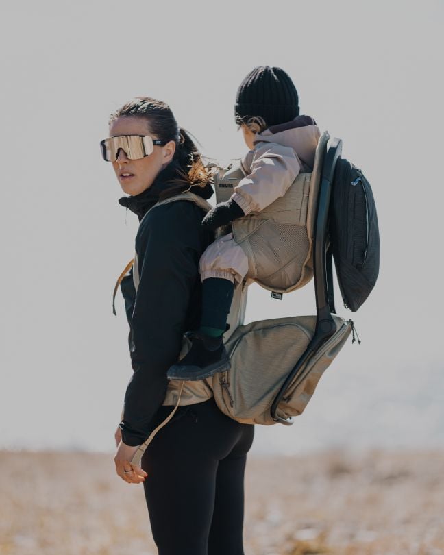 Parent carrying a child in a Thule child carrier backpack outdoors.
