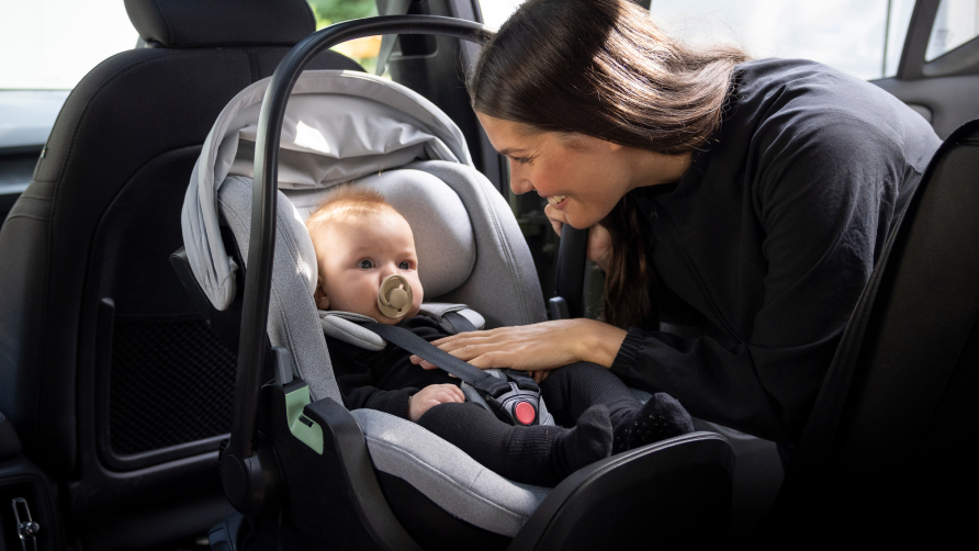 En kvinde kigger på sit barn, der sidder i en lysegrå Thule Maple-babyautostol.